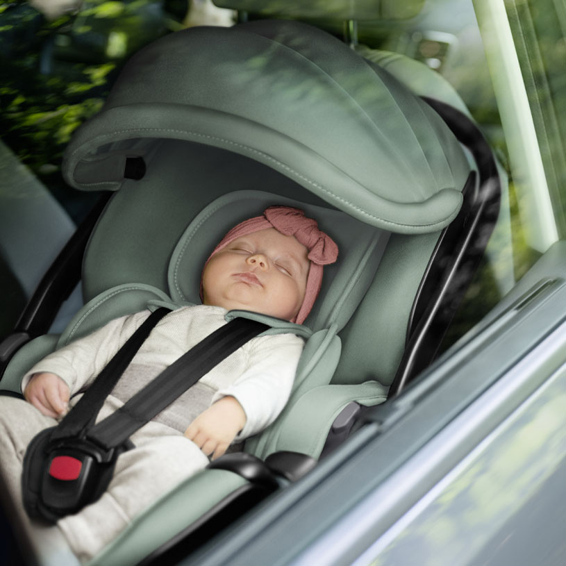 Bebis sover i bilbarnstol med rosa pannband.