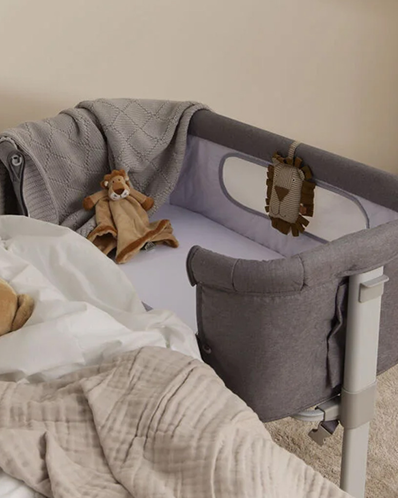 Grå sidosäng med gosedjur och filt i ett barnrum.