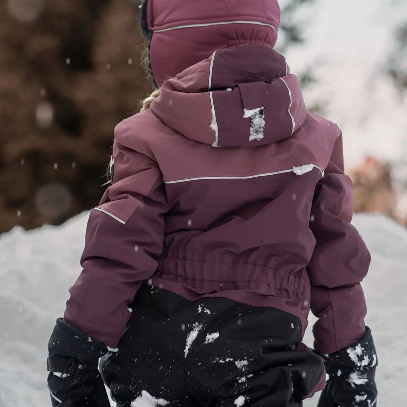 Barn i vinterkläder sitter i snön vid ett trästaket.