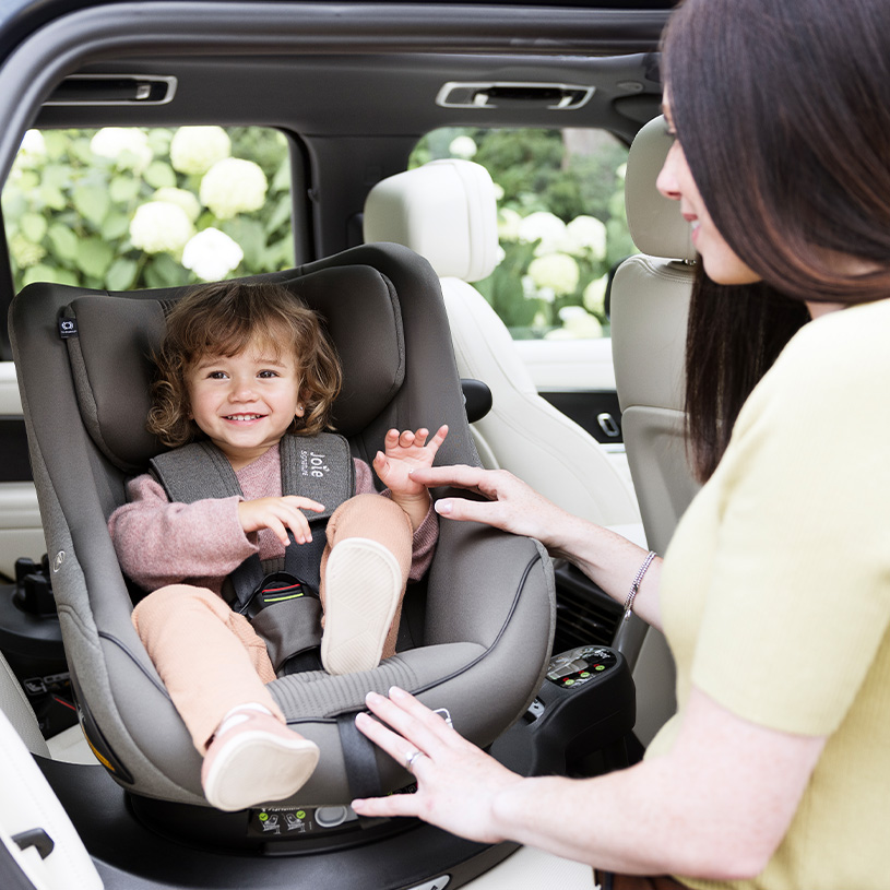 Barn i bilbarnstol med vuxen som justerar bältet.