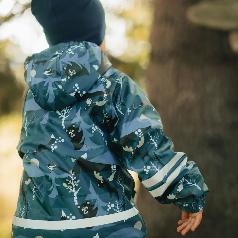 Barn i mönstrad overall leker vid vattenkant.