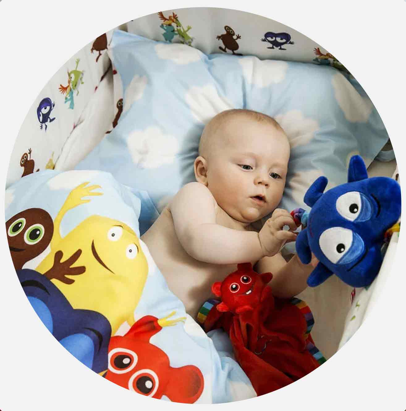 Baby leker med blå leksak i babysäng med färgglada kuddar.