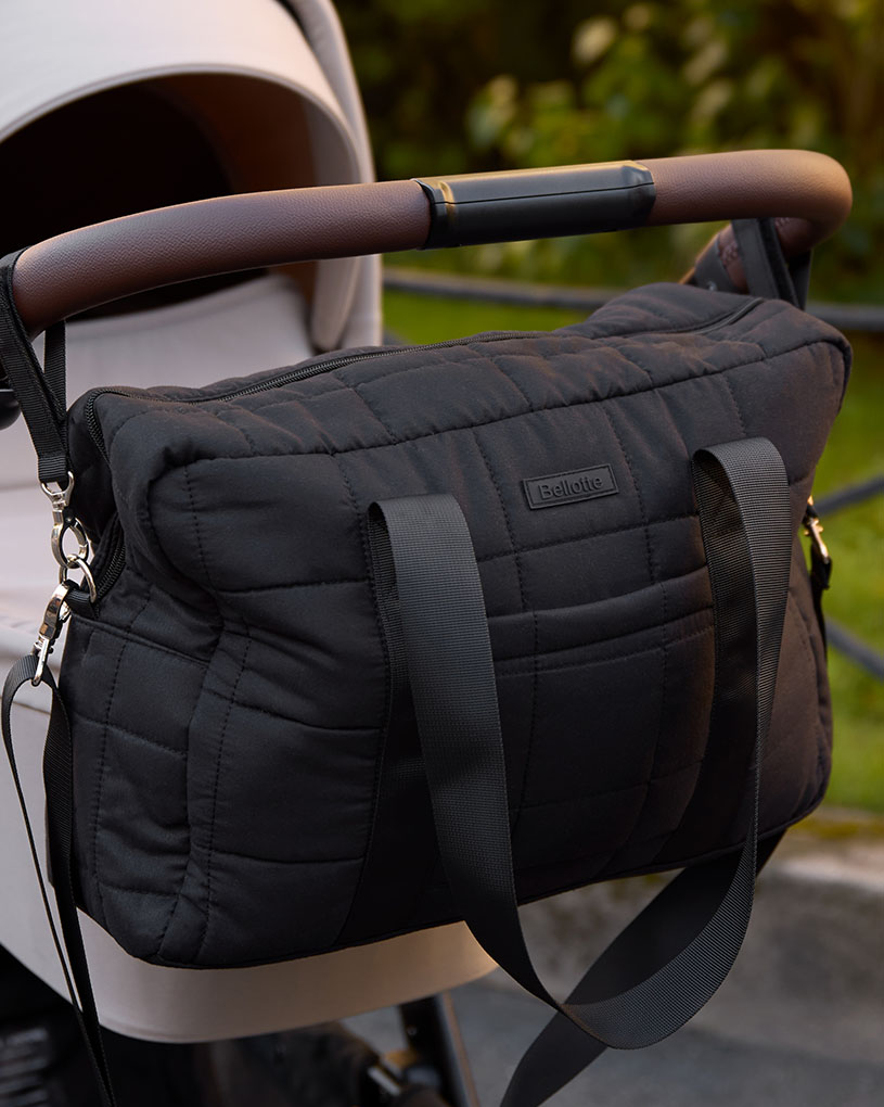 Svart mönstrad väska hänger på barnvagnens handtag utomhus.