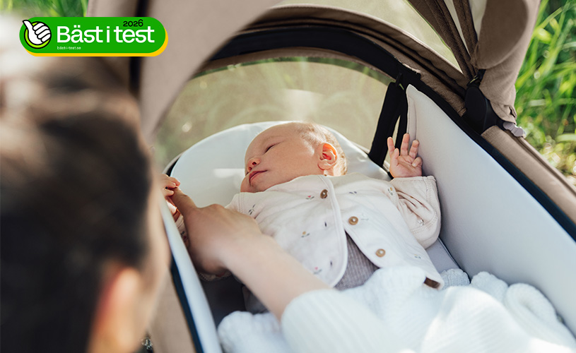 En baby ligger i en barnvagn, medan en vuxen rör vid babyns hand.