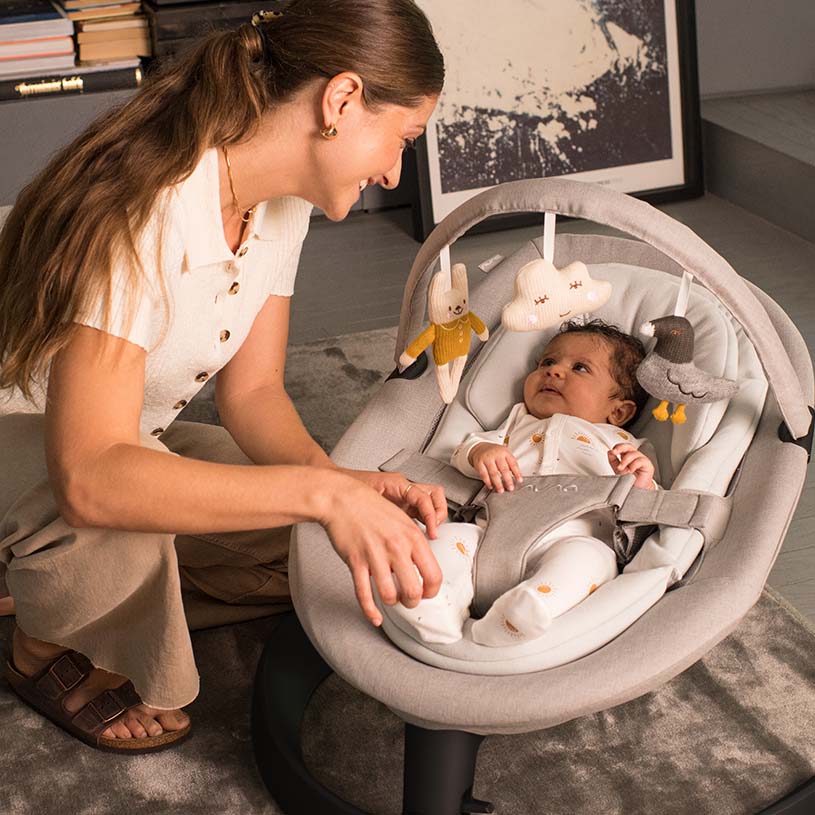 Kvinna ler mot bebis i babysitter med leksaker.