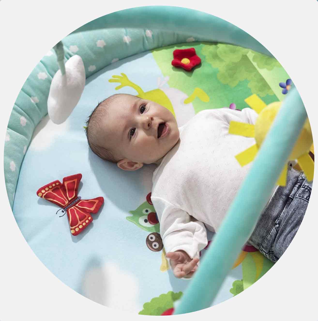 Bebis ligger på färgglad lekmatta med blommor och fjäril.