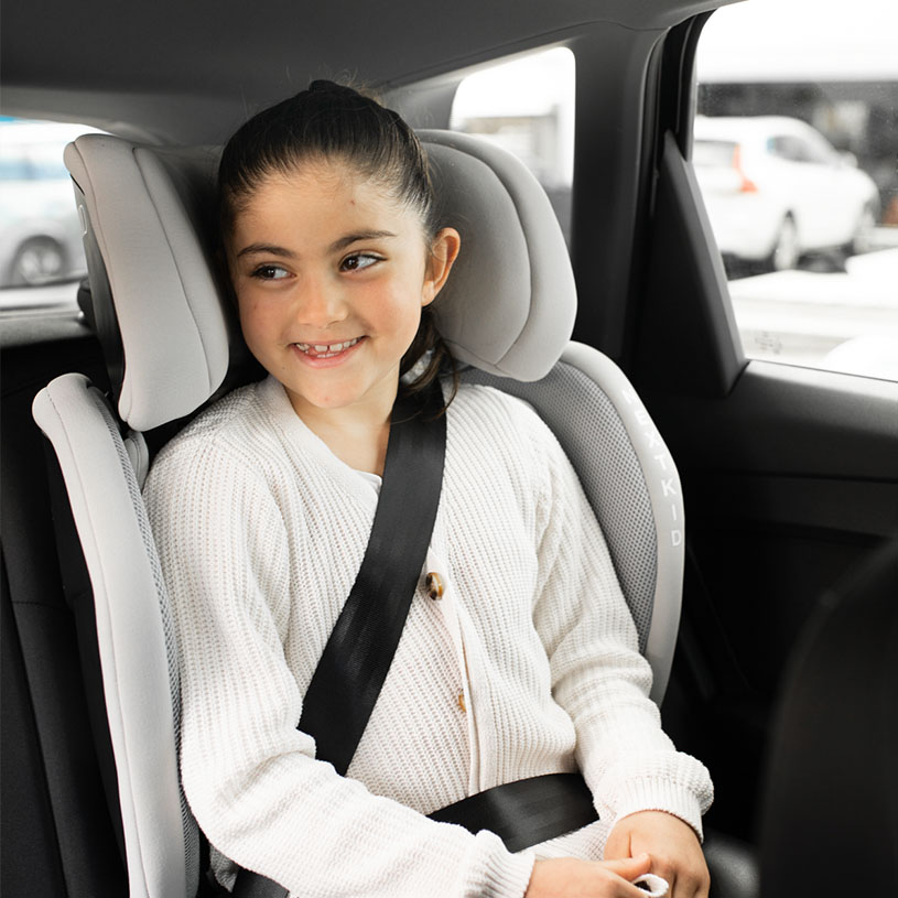 Barn i bilstol med bälte, ler.