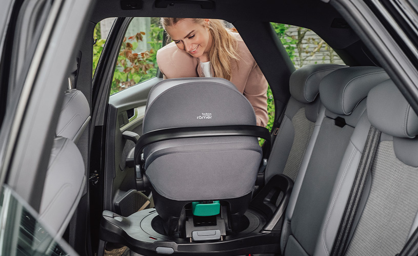 Kvinna installerar en bilstol med texten 'Britax Römer'.