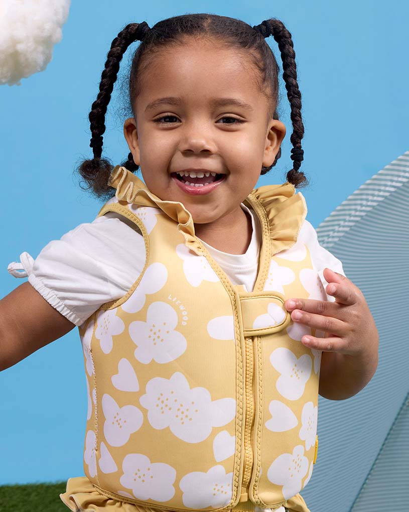 Barn med blont hår och flytväst med måsmotiv sitter vid poolen.