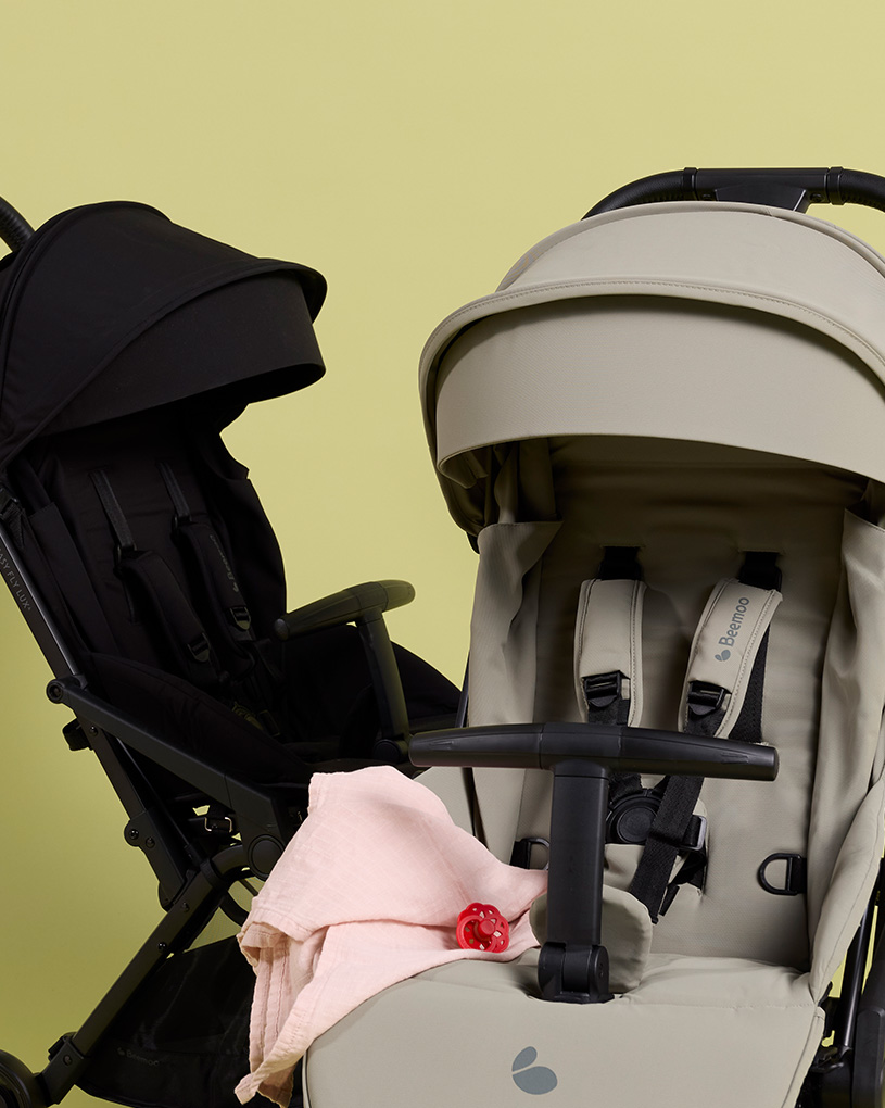 Två barnvagnar, en svart och en grå, med en napp och en rosa filt, med texten 'Sulkys'.