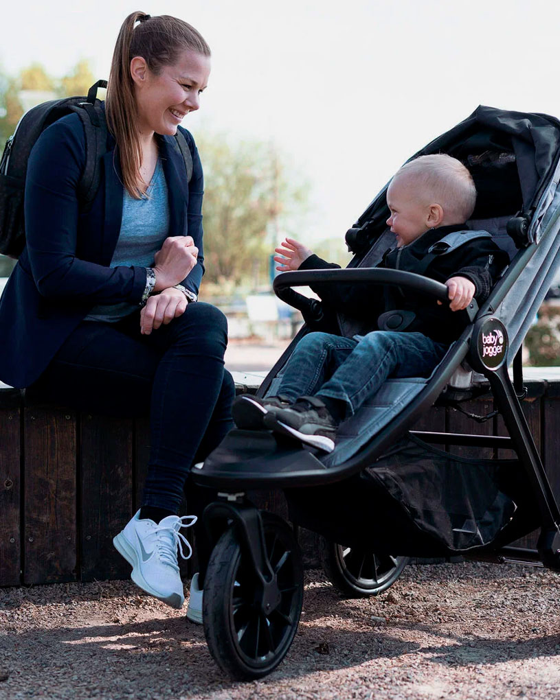 Kvinna ler mot barn i barnvagn utomhus.