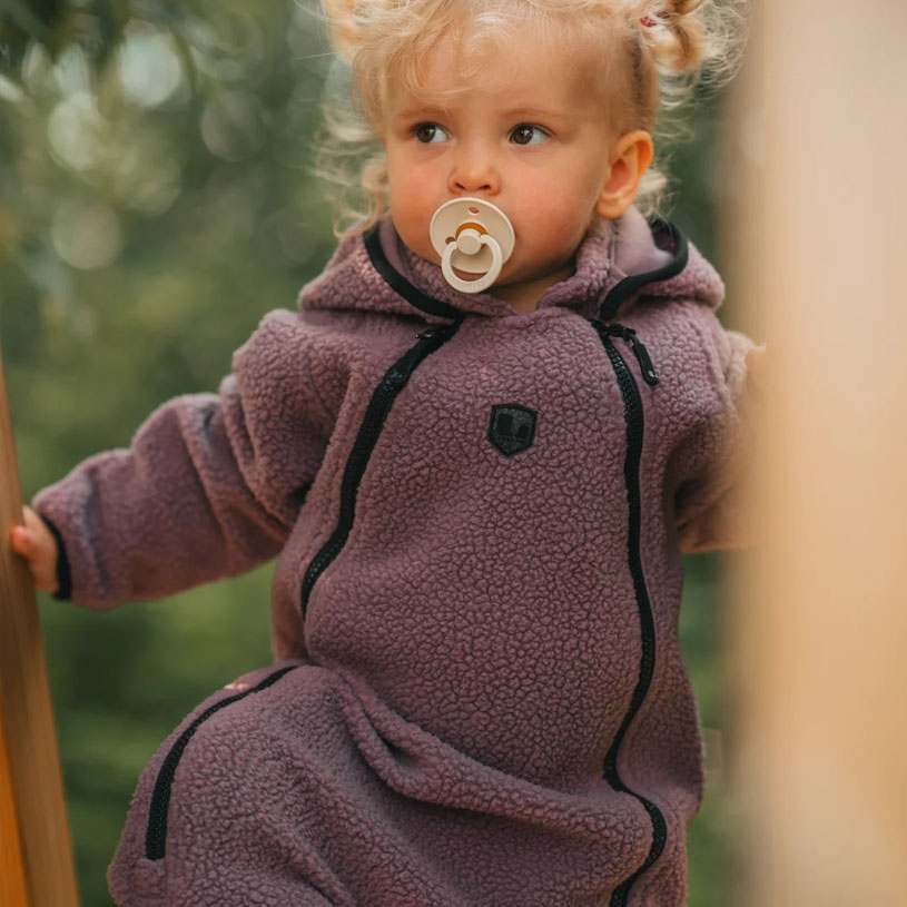 Bebis i rosa kläder gungar och ler i en blå gunga utomhus.