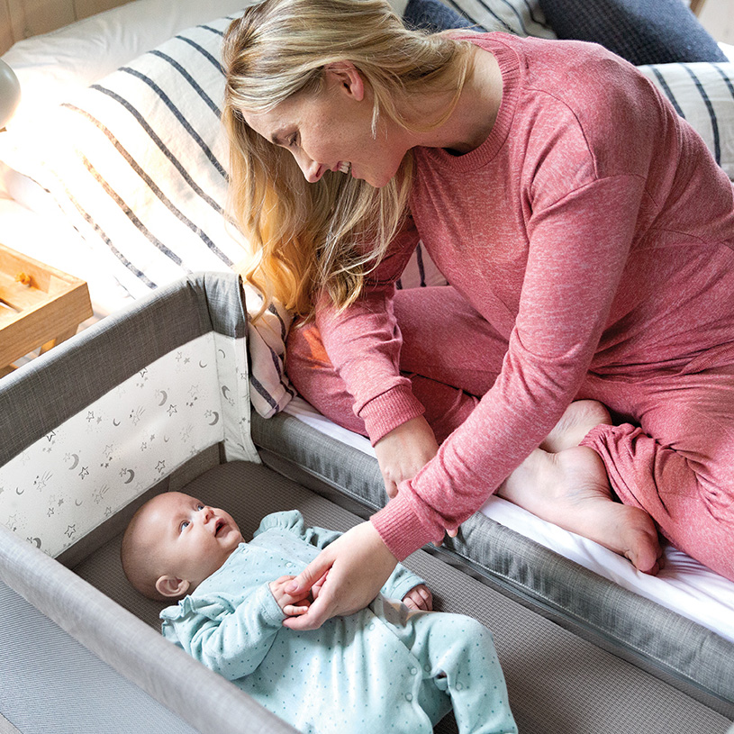 Bebis i gunga med leksaker, flicka sitter vid bord i bakgrund.