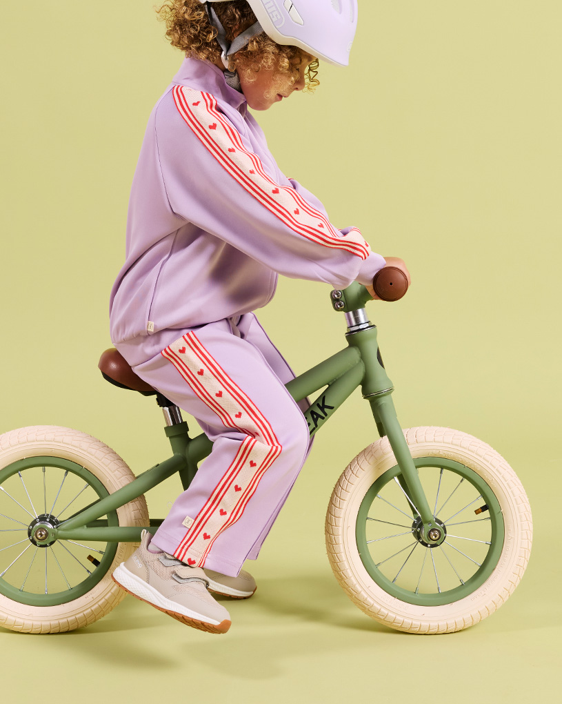Barn cyklar på en balanscykel i lila kläder med texten 'PEAK'.