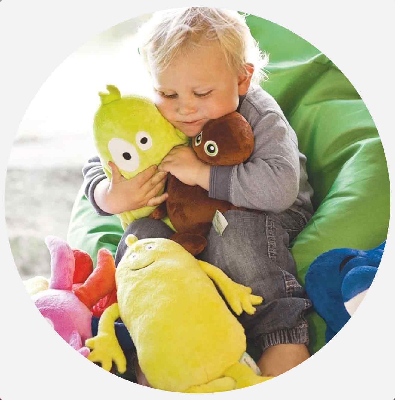 Litet barn kramar två färgglada gosedjur och sitter på en grön saccosäck.