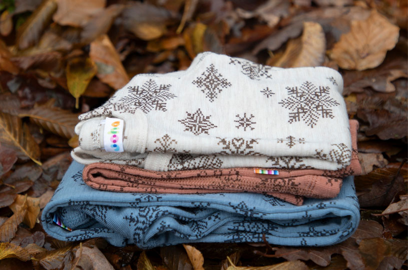 Tre hopvikta filtar med snöflingemönster ligger på höstlöv.