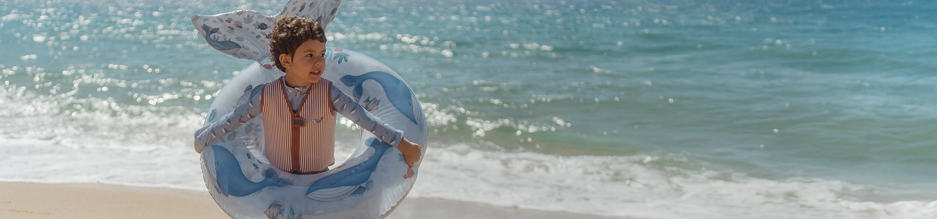 Barn på strand med badring, hav i bakgrunden. Text: "Nytt för säsongen".