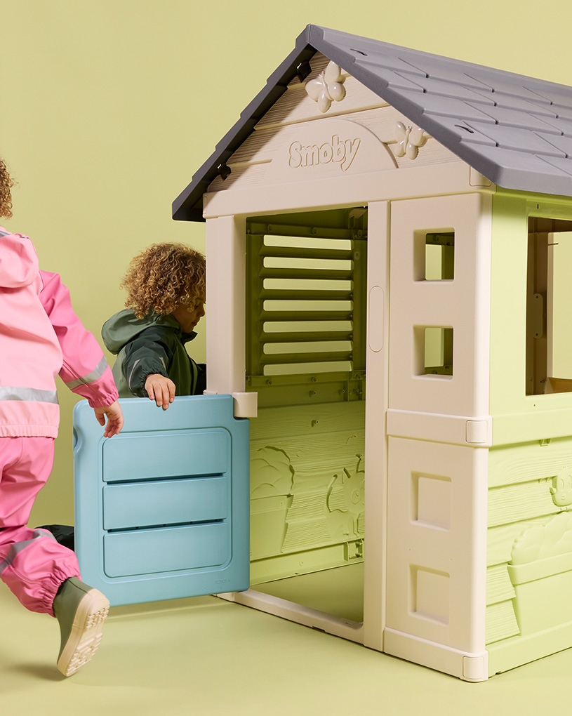 Barn leker vid ett lekstuga med texten 'Smoby'.