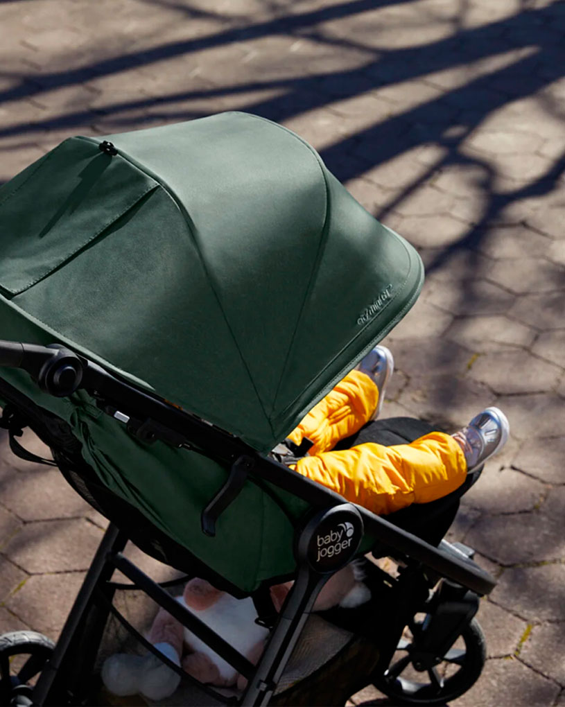 Barnvagn med grönt tak och barn i gula byxor.