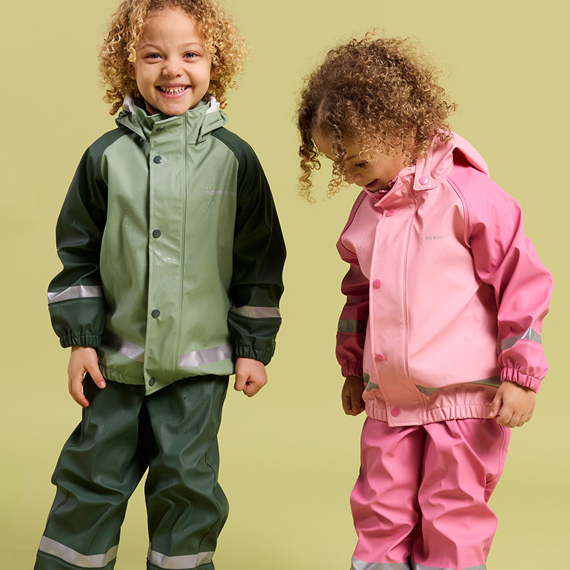 Två barn i regnkläder leker vid vattnet.