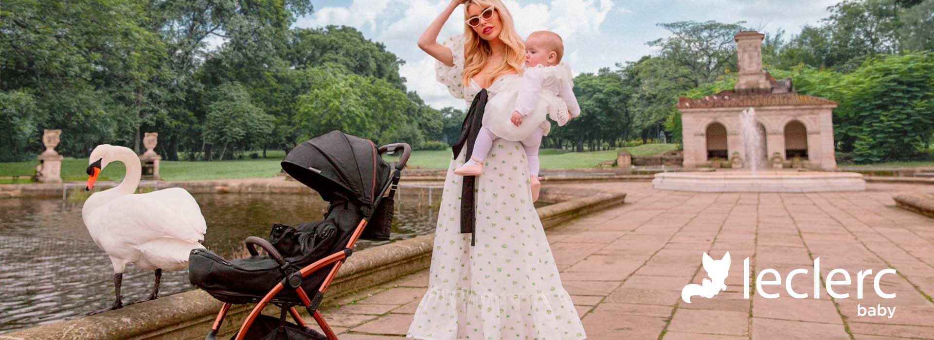 Kvinna med barn och barnvagn vid damm bredvid en svan.