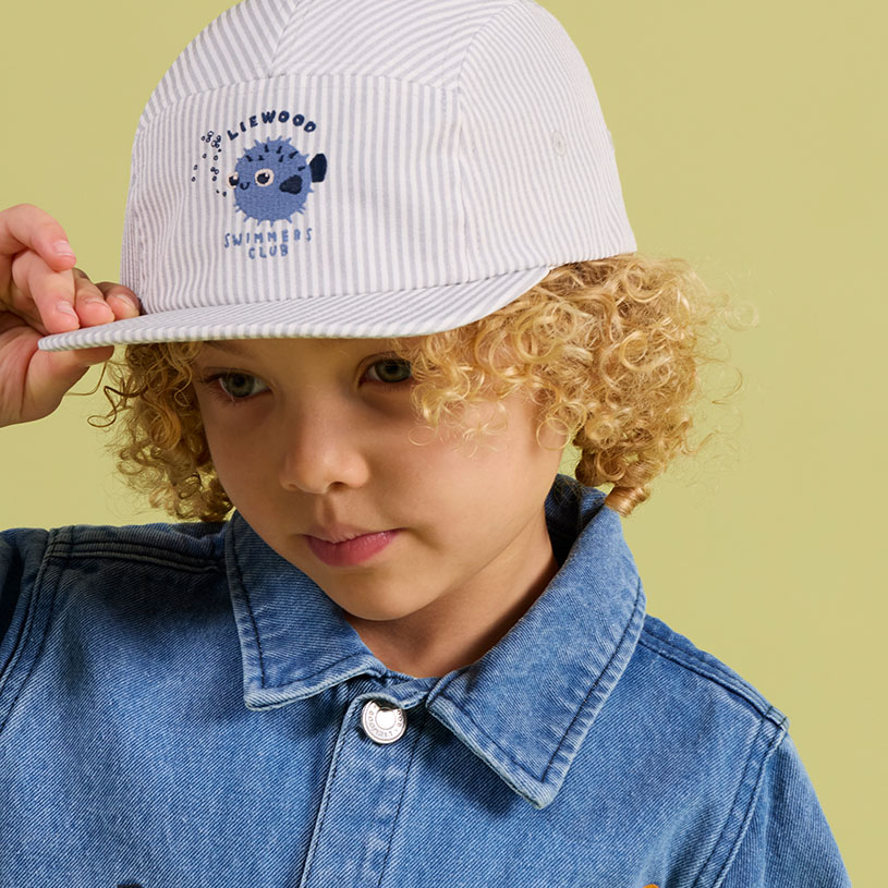 Person i grön jacka och blå keps med björn- och tallmotiv.