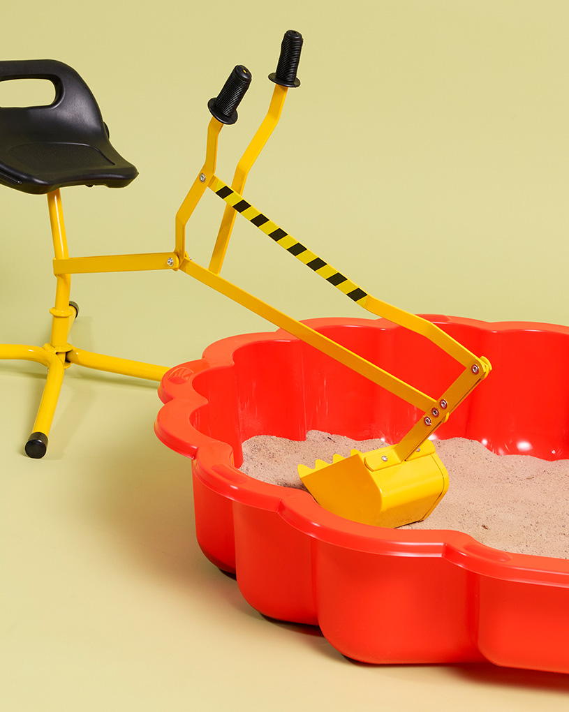 Röd sandlåda med en gul grävmaskin och en svart stol, med texten 'Utelek'.