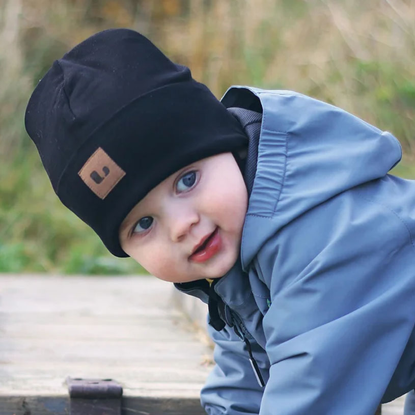 Barn i svart mössa och jacka ler utomhus.