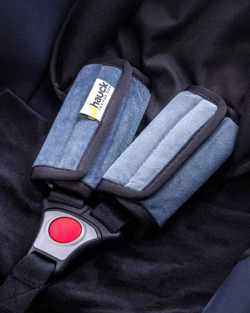 Närbild på bilbarnstol med blå vaddering och röd knapp.