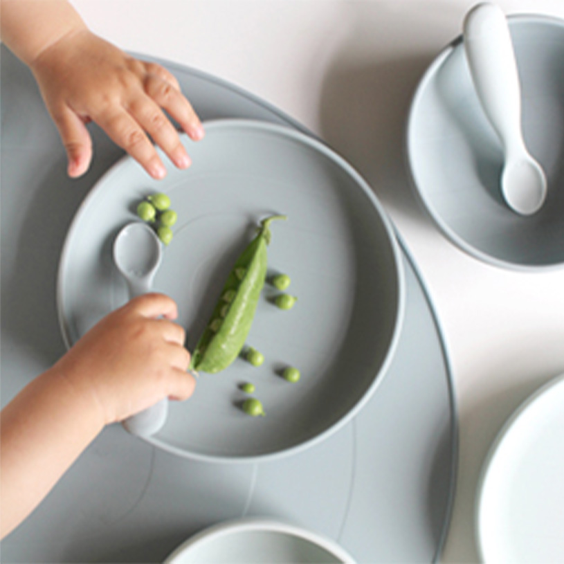 Barnhand rör vid ärtor på en grå tallrik med sked.